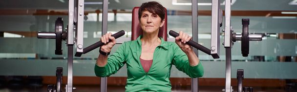 ισχυρή και παρακινούμενη ηλικιωμένη γυναίκα που γυμνάζεται στο γυμναστήριο, ώριμη φυσική κατάσταση, ενέργεια, ενεργός ηλικιωμένος, banner - Φωτογραφία, εικόνα