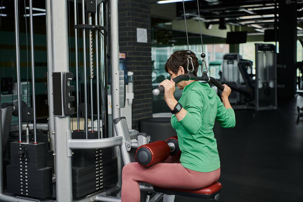 mujer mayor fuerte y motivada haciendo ejercicio en el gimnasio, fitness maduro, máquina de ejercicio, activo - Foto, Imagen