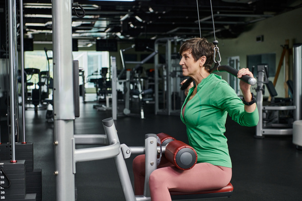 спортивна і мотивована літня жінка, що працює в спортзалі, зріла фітнес, тренажерний зал, вид збоку - Фото, зображення