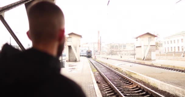 若い男が駅を出る電車を見ている. 駅を出発する列車を見ている若者の肖像画. - 映像、動画