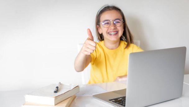 Söpö koulutyttö, jolla on kannettava tietokone keittiössä, opiskelee tietokoneella, nauttii verkko-oppimisesta. - Valokuva, kuva
