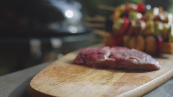 Primer plano enfoque selectivo de las manos del hombre colocando filetes de carne cruda en el tablero de madera en la mesa - Metraje, vídeo