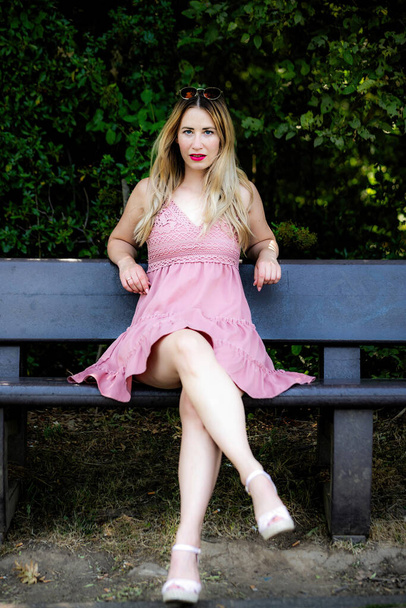 une jeune jolie femme aux cheveux blonds assise sur un banc dans le parc de la ville - Photo, image