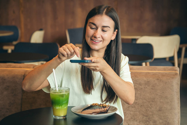 Mujer joven atractiva desayunando en el café en el interior, tomando una foto, blogueando. - Foto, Imagen