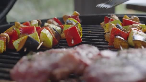Közelkép kézi kamera lövés fordult vega nyársak a BBQ fém fogóval, miközben grillezés őket marhahús steak - Felvétel, videó
