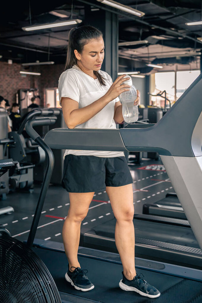 Egy nő egy üveg vízzel edzés közben, egészséges nő, futógépen edz.. - Fotó, kép