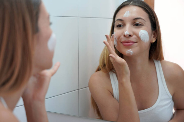Mujer de belleza aplicando crema en su piel. Tratamientos hidratantes hidratantes para la cara. Disfrutando de un tiempo relajante en casa. - Foto, Imagen
