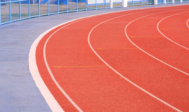 Prázdné červené zatáčky syntetické běžecké tratě s betonovou dlažbou a plotem na atletickém venkovním stadionu - Fotografie, Obrázek