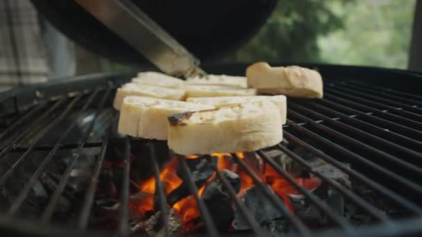 Κοντινό πλάνο των χεριών του αγνώριστη άνθρωπος στροφή φέτες ψωμιού στο μπάρμπεκιου σχάρα με μεταλλικές λαβίδες - Πλάνα, βίντεο