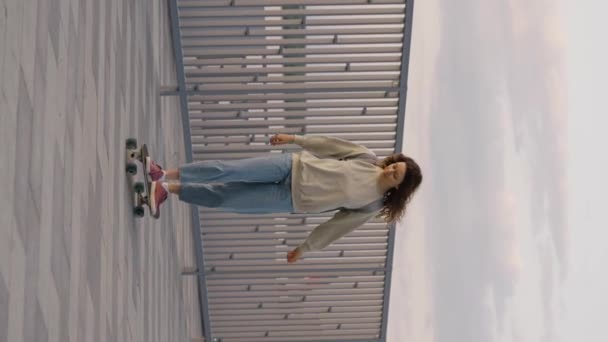 Fiatal gondtalan nő gördeszkázik végig a sétányon, függőleges videó. Stílusos hipster lány lovagol egy longboard egy hátizsák. - Felvétel, videó