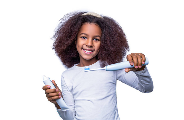 Μικρό κορίτσι, οδοντόβουρτσα. Πολυφυλετική κοπέλα βουρτσίζει τα δόντια της με ηλεκτρική οδοντόβουρτσα. Κοντινό πλάνο οδοντόβουρτσας για μικρά κορίτσια. Μικρή χαριτωμένη Αφροαμερικανή που βουρτσίζει τα δόντια της. Υγιή δόντια, οδοντόκρεμα. - Φωτογραφία, εικόνα