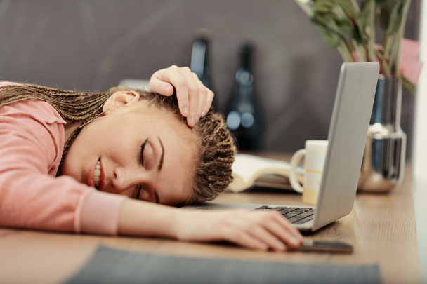 Erschöpft von der Arbeit oder dem Studium schläft eine Frau mit Zöpfen an ihrem Laptop ein, die Hand am Telefon - Foto, Bild