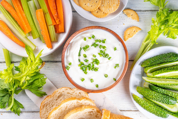 Hüttenkäse-Dip mit hohem Eiweißanteil mit frischem Gemüse, Brot und Crackern auf einem hölzernen weißen Tisch. Ernährung gesunder Quarkaufstrich mit verschiedenen Snacks - Foto, Bild