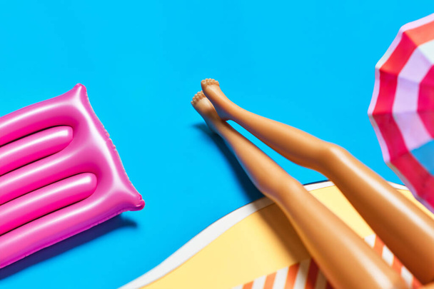 La muñeca está tomando el sol en una playa de juguetes, un colchón de aire y un paraguas. Concepto de fiesta de verano mínimo. Copiar espacio para texto - Foto, imagen