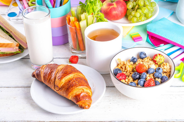 Gesundes, nahrhaftes Frühstück für Schulkinder mit frischem Obst, Gemüse, Croissant, Müsli, Milch und Sandwich. Frühstück vor der Schule und Arbeit, Kopierraum - Foto, Bild
