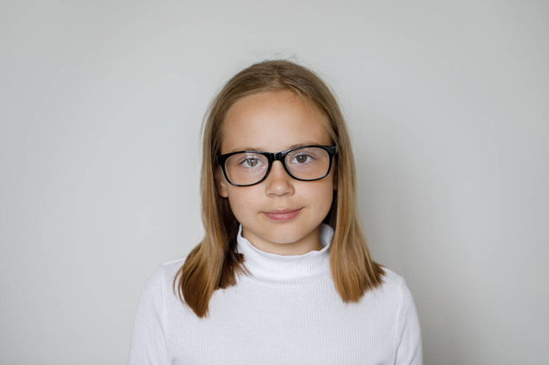 Умная девочка в очках смотрит в камеру на белом фоне, студийный портрет - Фото, изображение