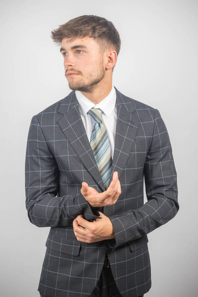 Portrait of a young entrepreneur in a suit and tie adjusting his cuffs against a plain background - Fotó, kép