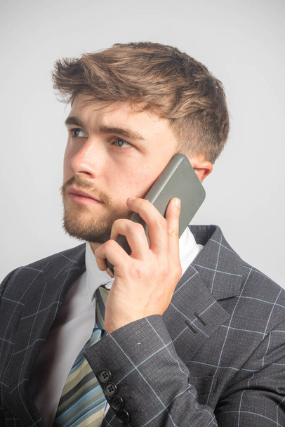 Egy fiatal vállalkozó portréja öltönyben és nyakkendőben mobiltelefonnal - Fotó, kép