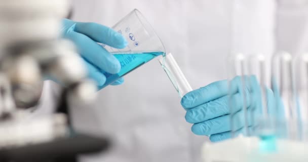 Käsineet kemisti kaatamalla sinistä nestettä pullosta koeputkeen laboratoriossa 4k elokuva. Lääketeollisuuden konsepti - Materiaali, video