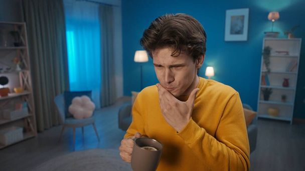 A man stands in the living room and holds his jaw with his hand close up. A man suffers from toothache after drinking hot tea. Tooth sensitivity, toothache. Home medicine concept - Fotó, kép