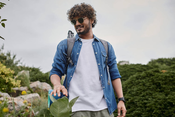 naturaleza salvaje, hombre indio feliz en gafas de sol caminando con mochila en la colina, excursionista teniendo viaje - Foto, imagen