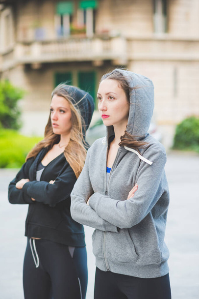 Twee jonge millennial sportieve vrouw dragen trainingspak buiten in de stad, armen gekruist. - Foto, afbeelding