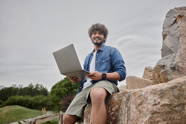 glücklicher indischer Freiberufler, der aus der Ferne arbeitet und Laptop am natürlichen Ort nutzt, digitaler Nomadentum - Foto, Bild