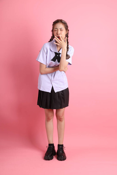 Das asiatische Mädchen in thailändischer Studentenuniform steht auf dem rosa Hintergrund. - Foto, Bild