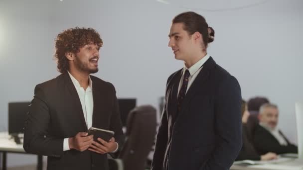 Resmi takım elbiseli iki genç adamın dijital tabletten bir şeye bakması. Bir finans şirketinin iki çalışanı mola sırasında iletişim kuruyor. Yüksek kalite 4k görüntü - Video, Çekim