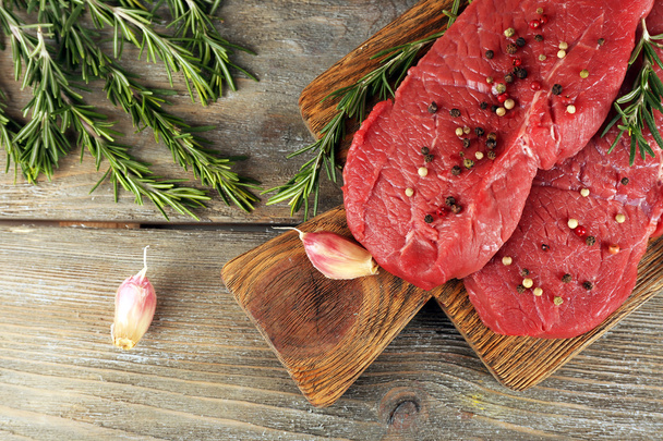 Raw beef steak with rosemary and garlic on cutting board on wooden background - Valokuva, kuva
