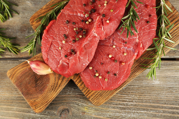 Raw beef steak with rosemary and garlic on cutting board on wooden background - Valokuva, kuva