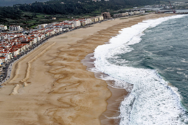 Город Назаре, Португалия - вид под скалами. Вид сверху на город Назаре и песчаный пляж. Самые большие волны в мире - в Назаре, округ Лейрия, Португалия - Фото, изображение