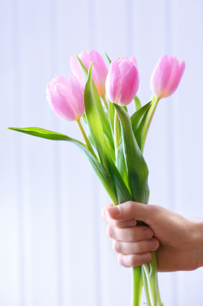 Hand holding beautiful pink tulips on wooden background - Foto, afbeelding