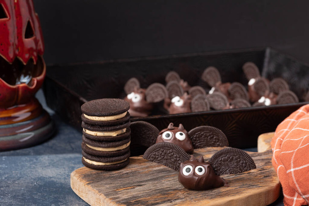 Met chocolade bedekte koekjes vleermuizen maken met grote ogen voor het Halloween feest. - Foto, afbeelding