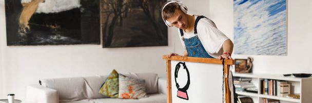 Young white man in headphones working on craft rug at home - Фото, изображение