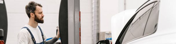 Bearded car mechanic testing car while working in garage indoors - Фото, зображення