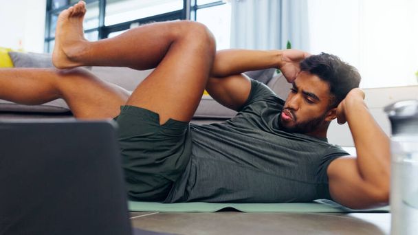 Fitness man, home workout και laptop, ενώ παρακολουθείτε online άσκηση φροντιστήριο στο σαλόνι στο σπίτι. Γυμνασμένος και δραστήριος άνθρωπος κάνει κοιλιακούς ενώ χρησιμοποιεί το διαδίκτυο για ένα blog υγείας και ευεξίας. - Φωτογραφία, εικόνα