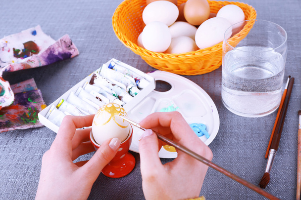Painting Easter eggs by female hands on colorful tablecloth background - Foto, afbeelding
