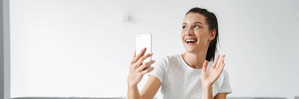 European smiling woman gesturing and taking selfie on mobile phone at home - Foto, Imagen