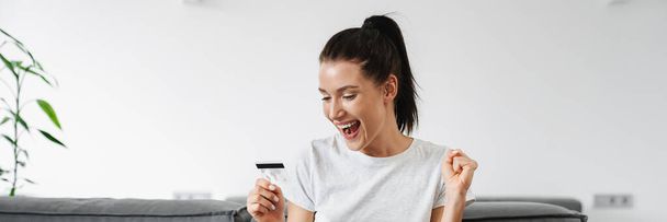 自宅でクレジットカードやノートパソコンを使用している間に勝者のジェスチャーを作る興奮した女性 - 写真・画像