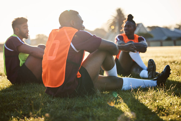 Rugby, tiimi ja miehet rentoutuvat ulkona, puhuvat ja kommunikoivat auringonnousun aikaan. Urheilu, urheilija ryhmä ja pelaajat istuvat ruohoa harjoituksen jälkeen, koulutusta tai ystäviä harjoitus peli. - Valokuva, kuva