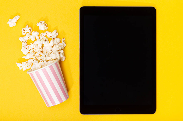 Secchio di popcorn e tablet bianco schermo nero su sfondo giallo. Vista dall'alto - Foto, immagini