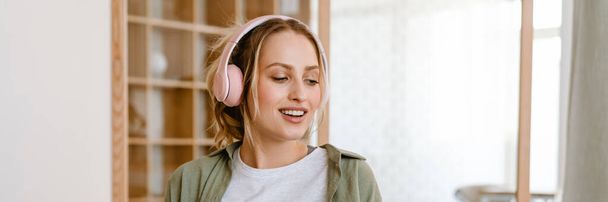 Young woman smiling while listening music with cellphone and headphones at home - Fotografie, Obrázek