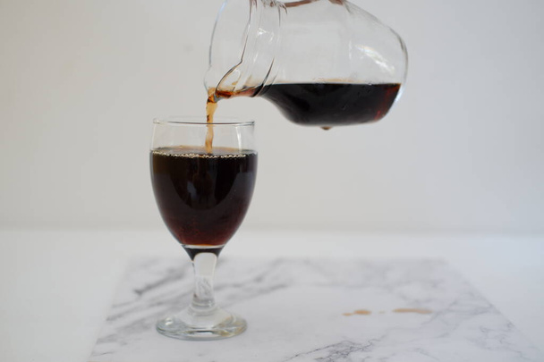 Verser le cola d'une cruche dans un verre sur un fond blanc - Photo, image