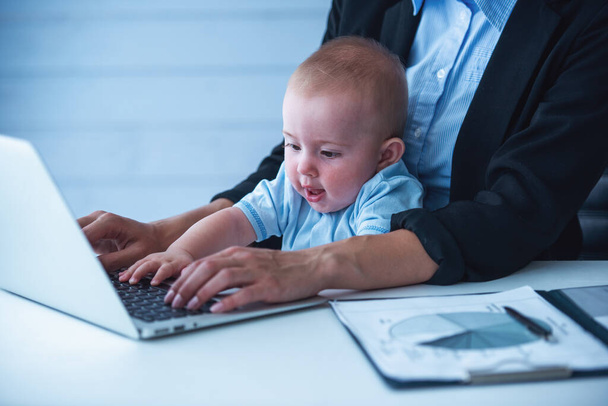 Suloinen vauva leikkii kannettavalla tietokoneella ja hymyilee istuessaan äitinsä polvilla.
 - Valokuva, kuva