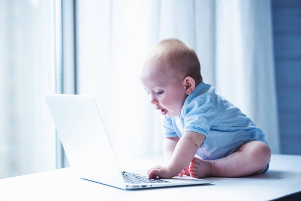 Lindo bebé está jugando con el portátil mientras está sentado en el escritorio
 - Foto, imagen