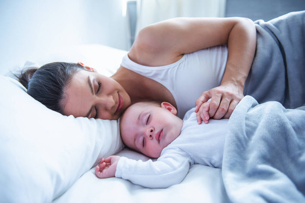 Seitenansicht der schönen jungen Mutter mit ihrem süßen kleinen Baby, das zu Hause im Bett schläft - Foto, Bild