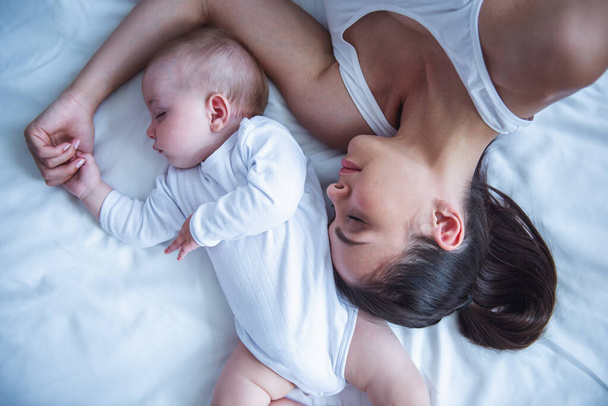 Вид сверху на красивую молодую маму и ее милого маленького ребенка, спящего в постели дома
 - Фото, изображение