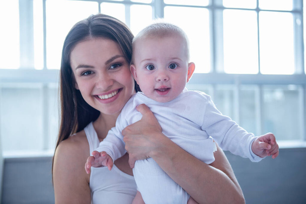 Πορτρέτο του όμορφη νεαρή μητέρα και γλυκό μικρό μωρό βλέπει κάμερα και χαμογελαστός - Φωτογραφία, εικόνα