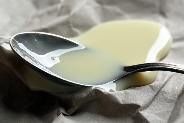 Spoon with condensed milk on paper background - Photo, image